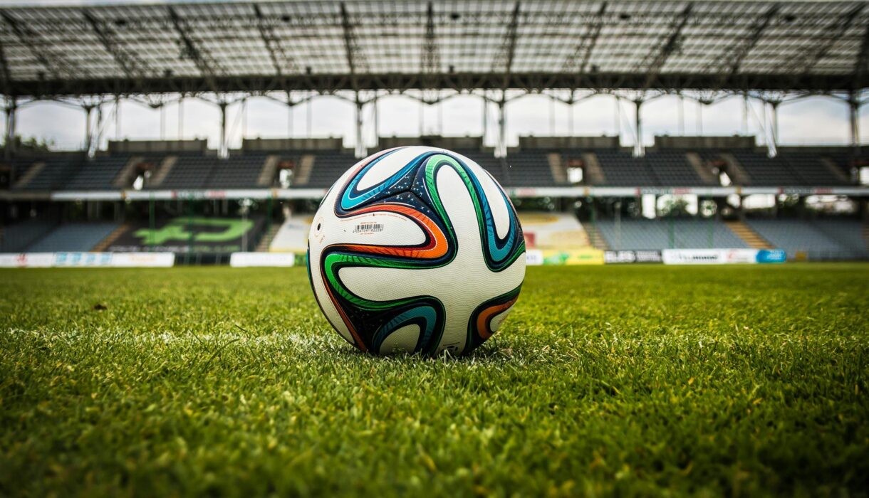 A vibrant soccer ball rests on a lush green field inside an empty stadium, capturing the essence of sports.